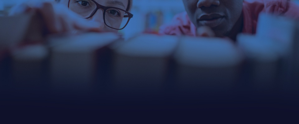 Two students overlooking books in the stacks. 