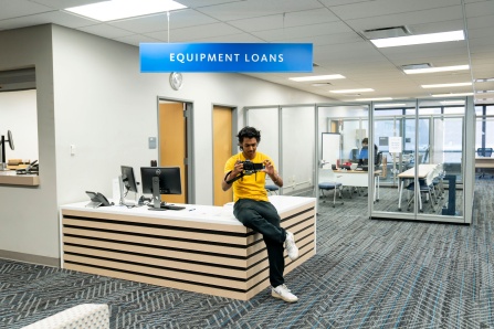 Photo of a student testing out a camera at the Equipment Loans desk. 