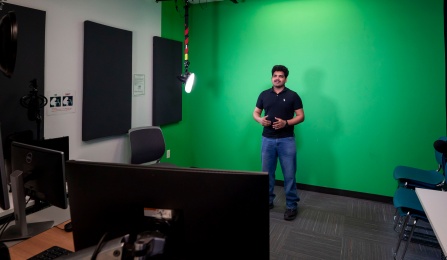 Photo of a student using the UB Libraries recording studio, equipped with cameras, computers, lighting, audio equipment, and more. 