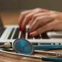 Photo of hands typing on a computer next to a stethoscope. 