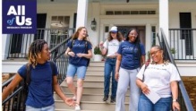 A diverse group of smiling young people talk as they exit a building and walk down the stairs. 
